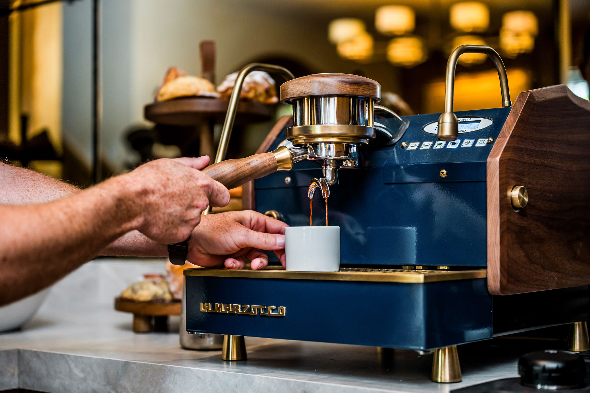 A barista pulling an espresso on the brass and navy machine at The Polo House