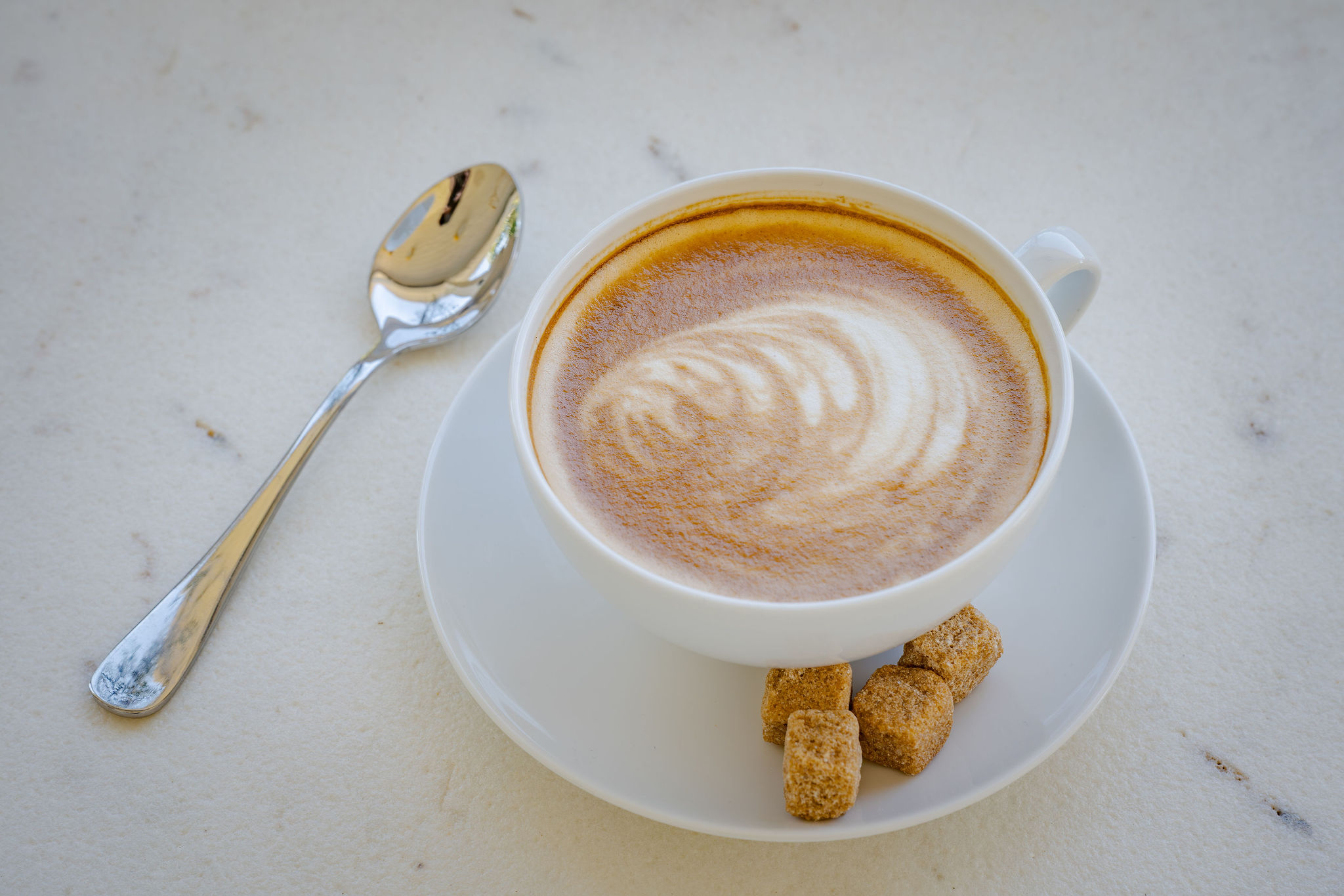 A latte with rosetta art and brown sugar cubes on a marble table at The Polo House