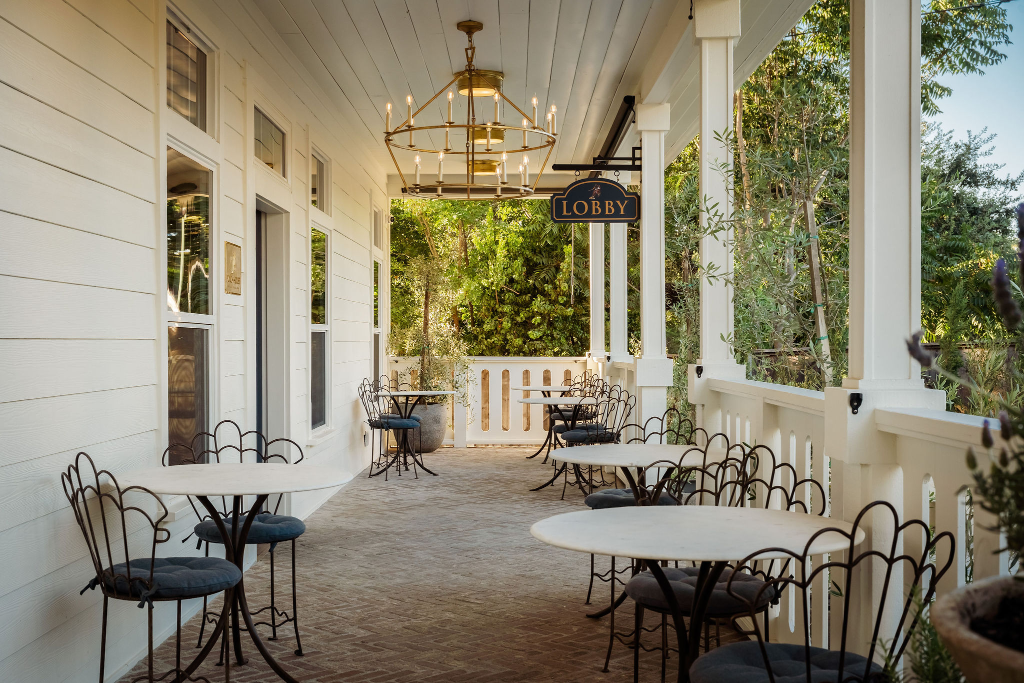 The porch with marble bistro tables beneath a brass chandelier at The Polo House